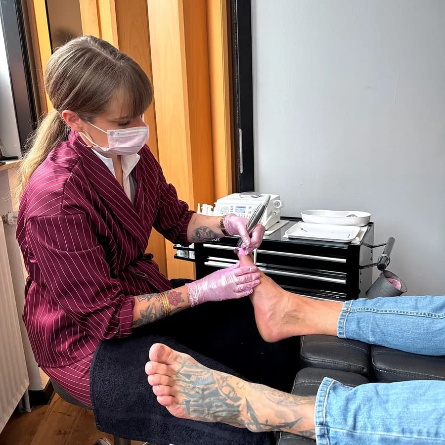 Pediküre: Mitarbeiterin mit Mundschutz und rosa Handschuhen behandelt den Fuß eines Kunden auf der Liege