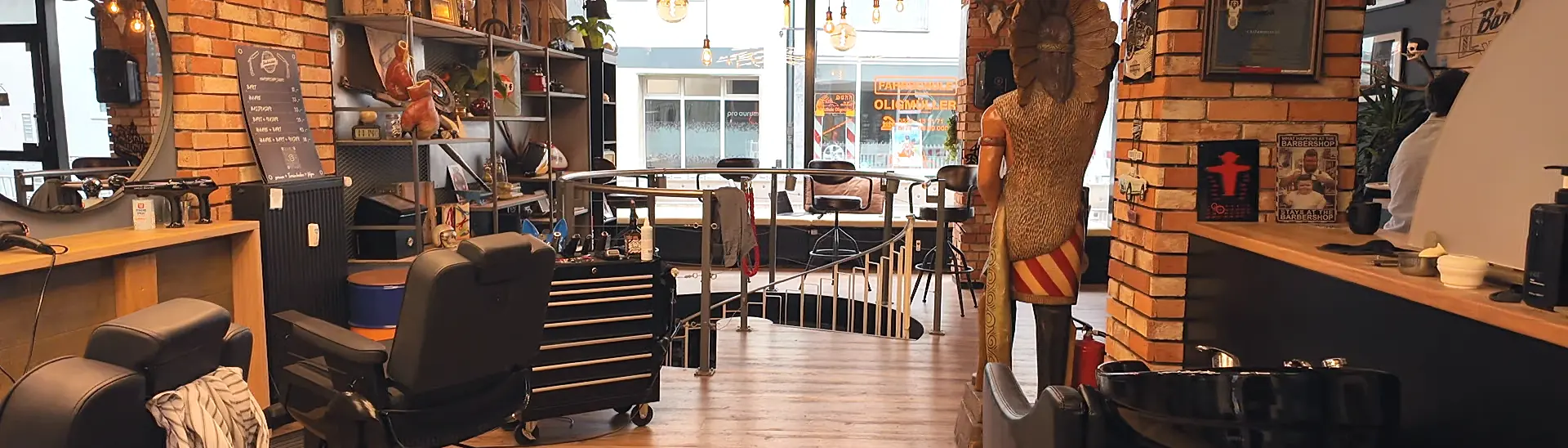 Vorderer Ladenbereich des Barbershop Sauer mit Barberstuhl, Werkzeugwagen, Wendeltreppe, Schaufenster und einer geschnitzten Holzfigur